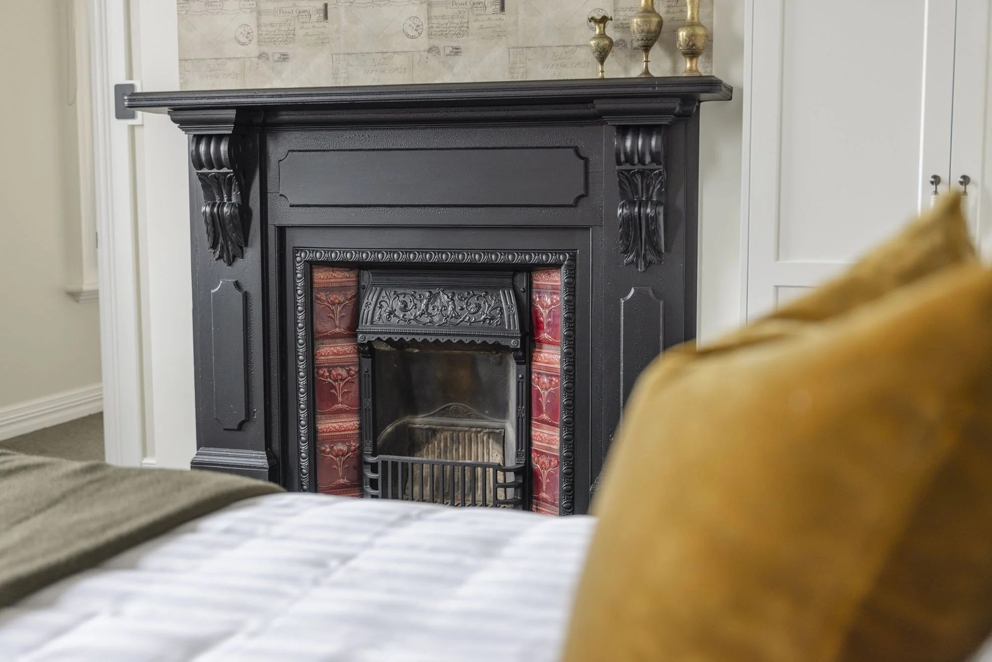 Living room with a black ornate fireplace, beige walls, and a mustard yellow couch in the foreground.