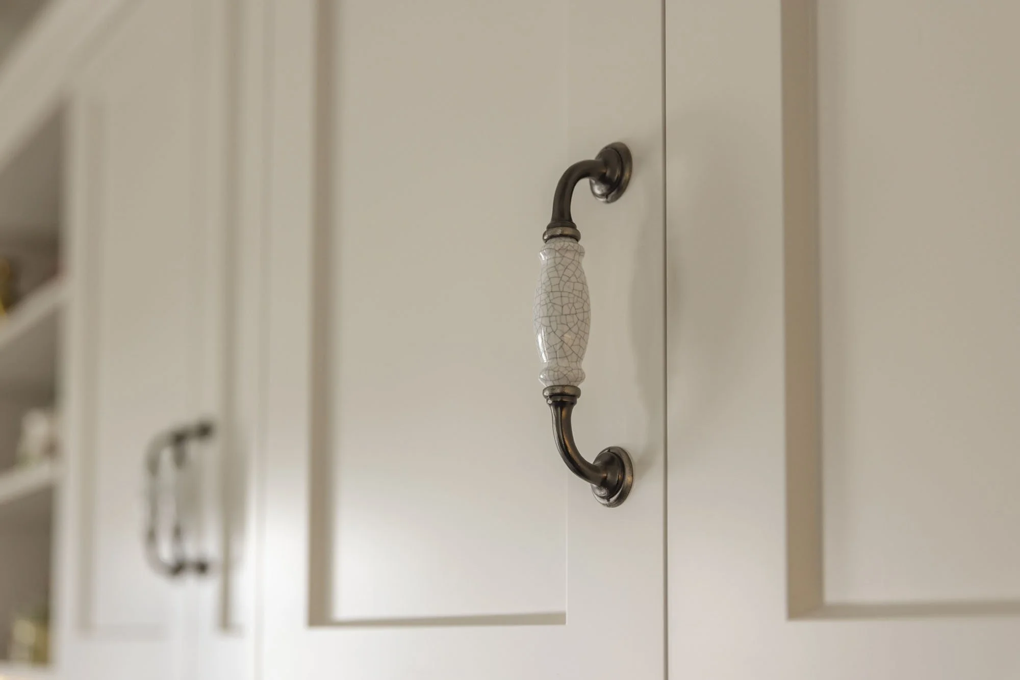 Close-up of a white cabinet door with a decorative ceramic and metal handle.