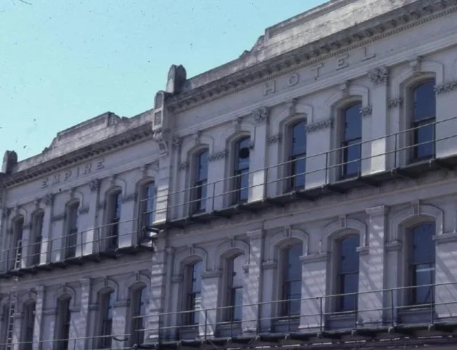Close-up view of a historic building with intricate architectural details, windows, and a fire escape, partially reflecting in the windows.