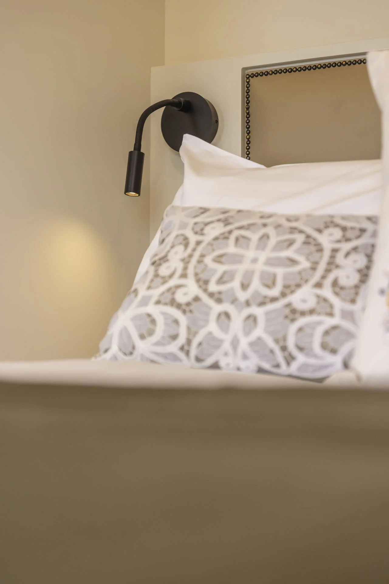 Close-up of a decorative pillow with a gray and white geometric pattern on a bed, next to a black wall-mounted reading light.