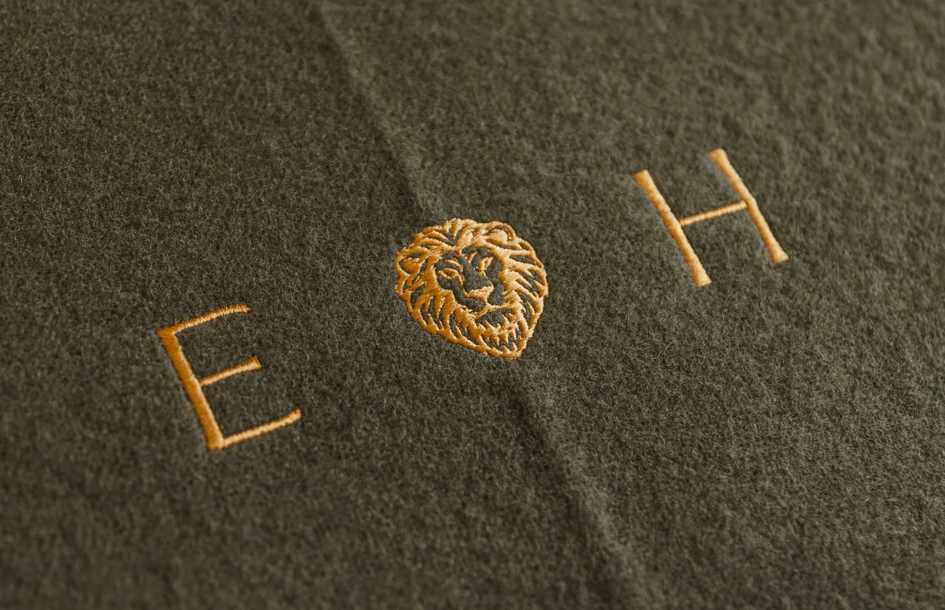 Close-up of dark fabric with embroidered orange letter 'E', a lion's face logo, and the letter 'H'.