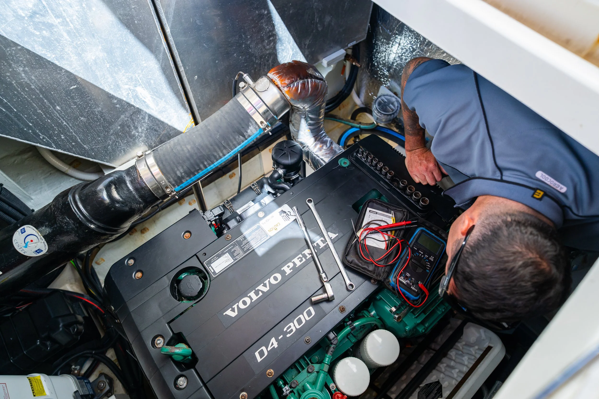 The image shows a person working on the engine compartment of a Volvo D4-300 engine, using tools and a testing device.