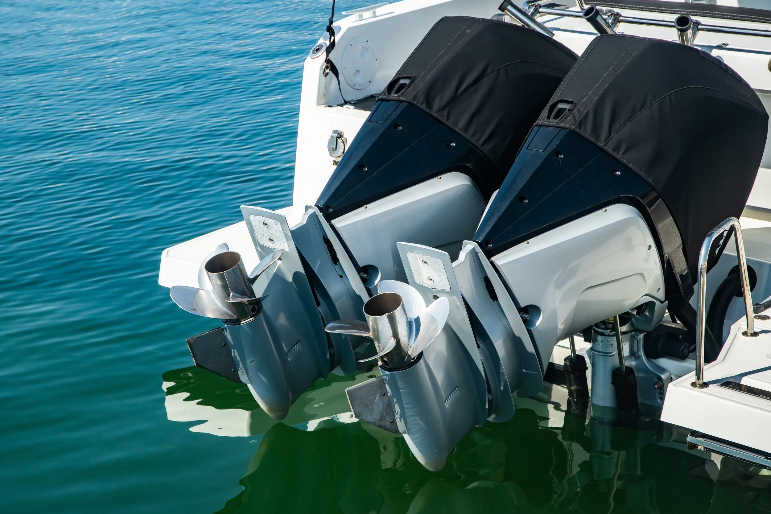 Close-up of two boat engines with black covers, mounted at the stern of a boat on calm water.