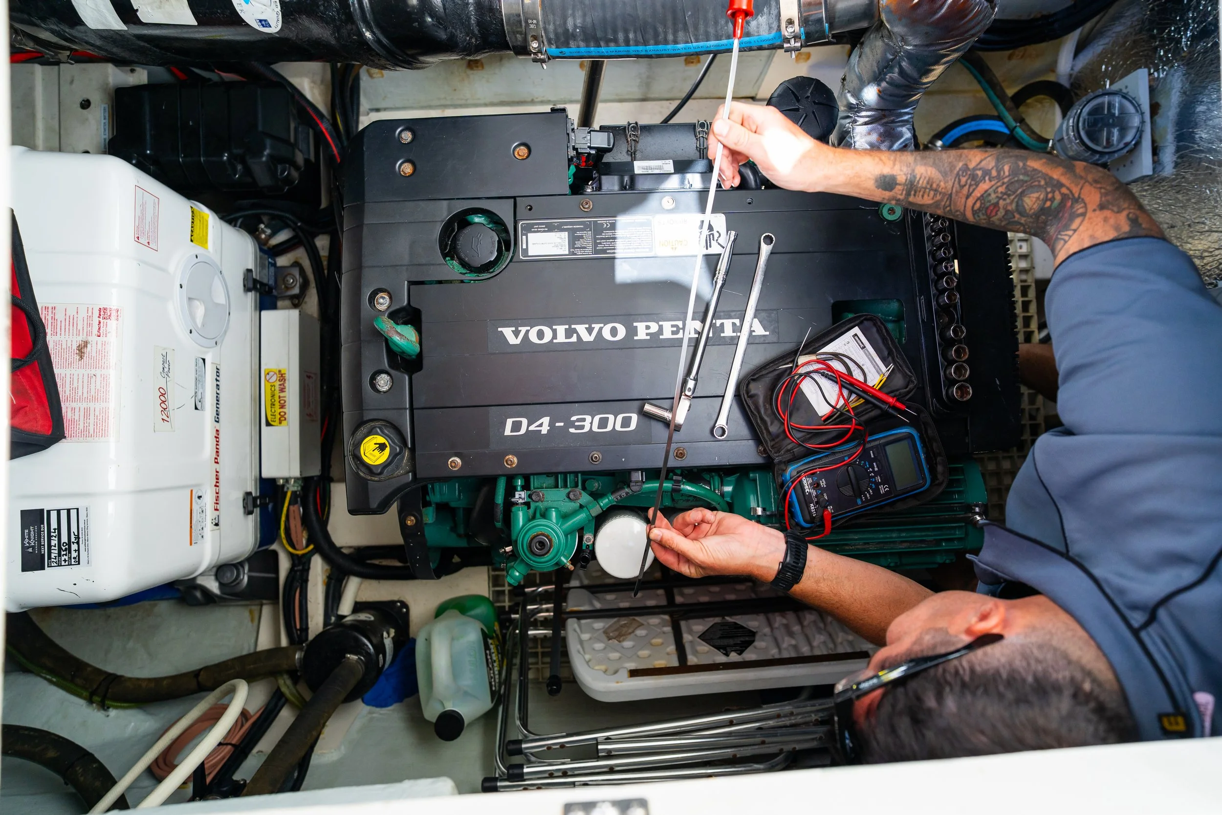 A technician working on a Volvo Penta marine engine, using tools to inspect or repair the engine inside a confined space.