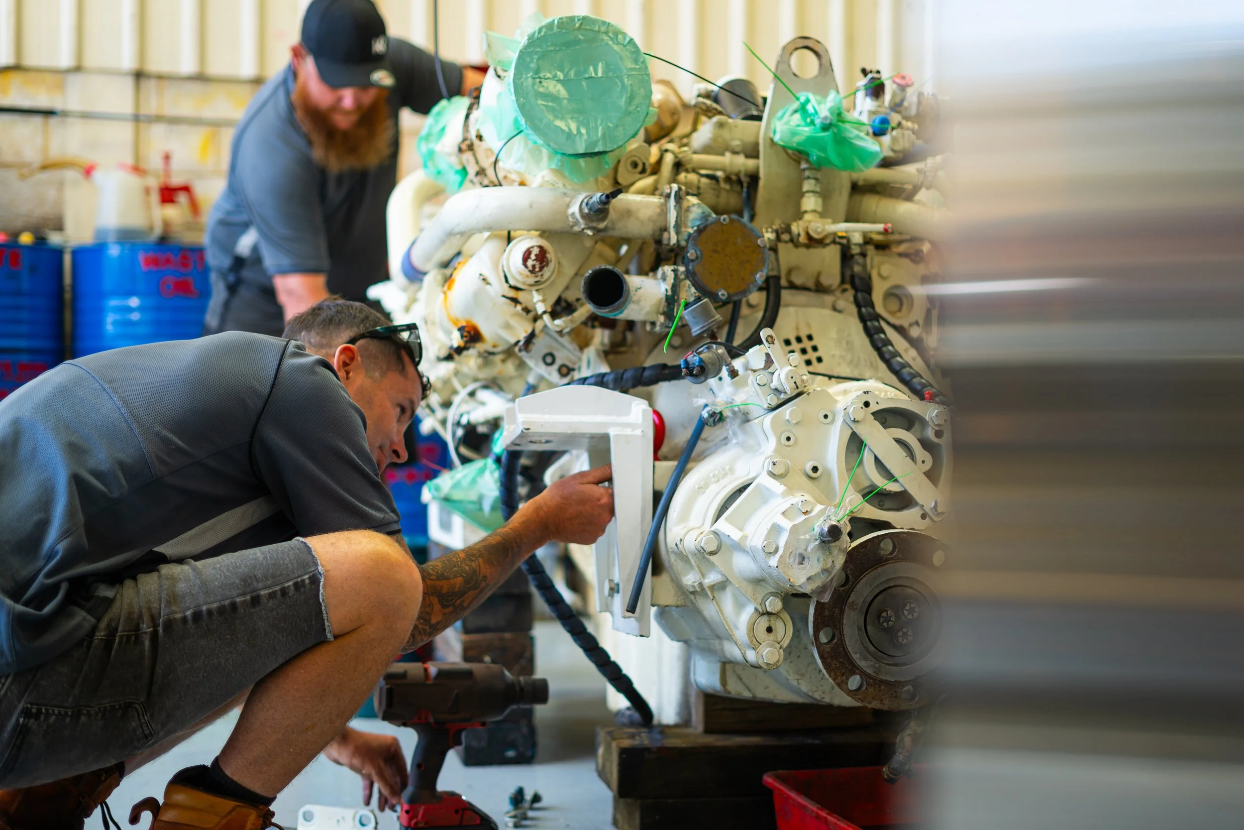 Two technicians work on assembling or repairing a complex mechanical or aerospace equipment, with one focused on a component and the other observing, in an industrial workshop.