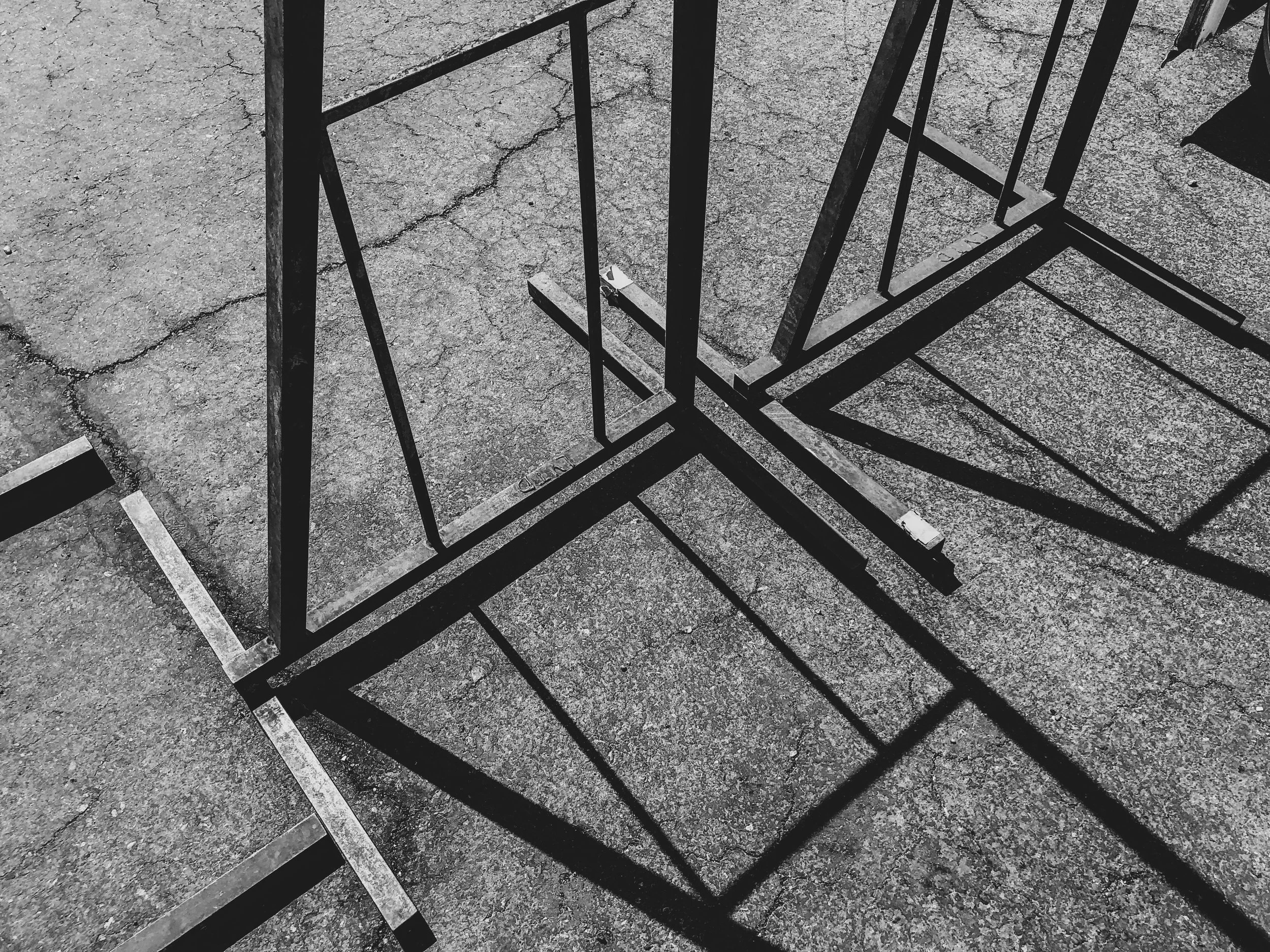 Black metal frames casting shadows on textured concrete ground.