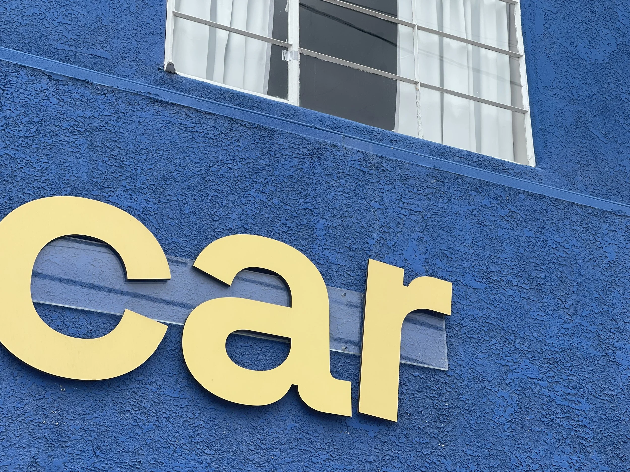 Close-up of a yellow sign with the partial word 'ear' mounted on a textured blue wall, with a window visible above.