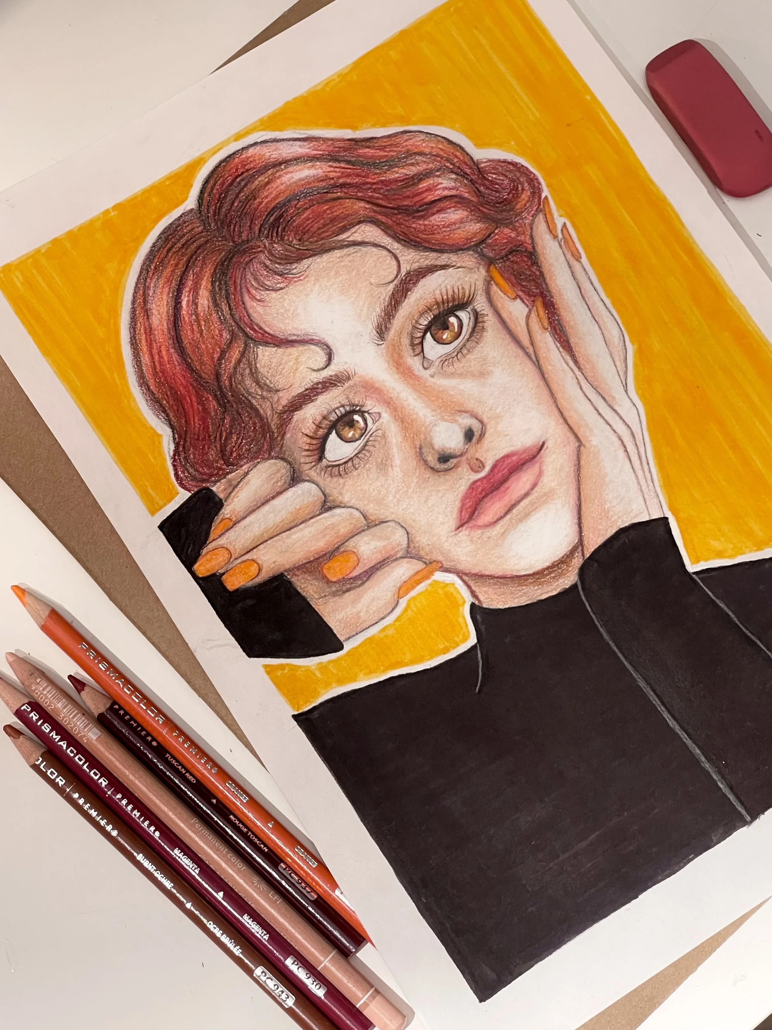 Colorful drawing of a young woman's face with brown eyes and curly red hair, holding her face with hands that have painted nails, set against a yellow background, with art supplies nearby.