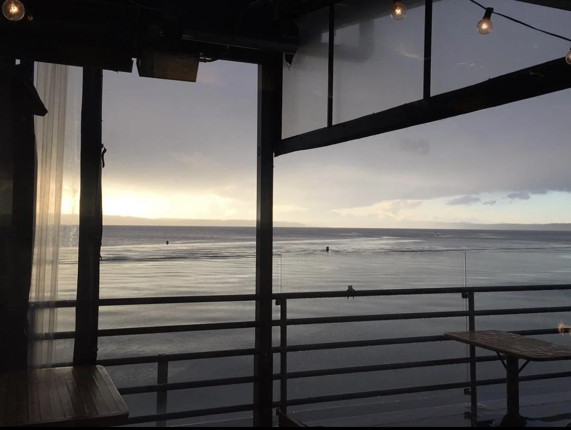 View from a balcony overlooking the ocean with a cloudy sky and a setting or rising sun.
