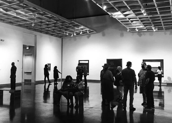 People viewing artwork and socializing in a modern art gallery with framed pictures on the wall.