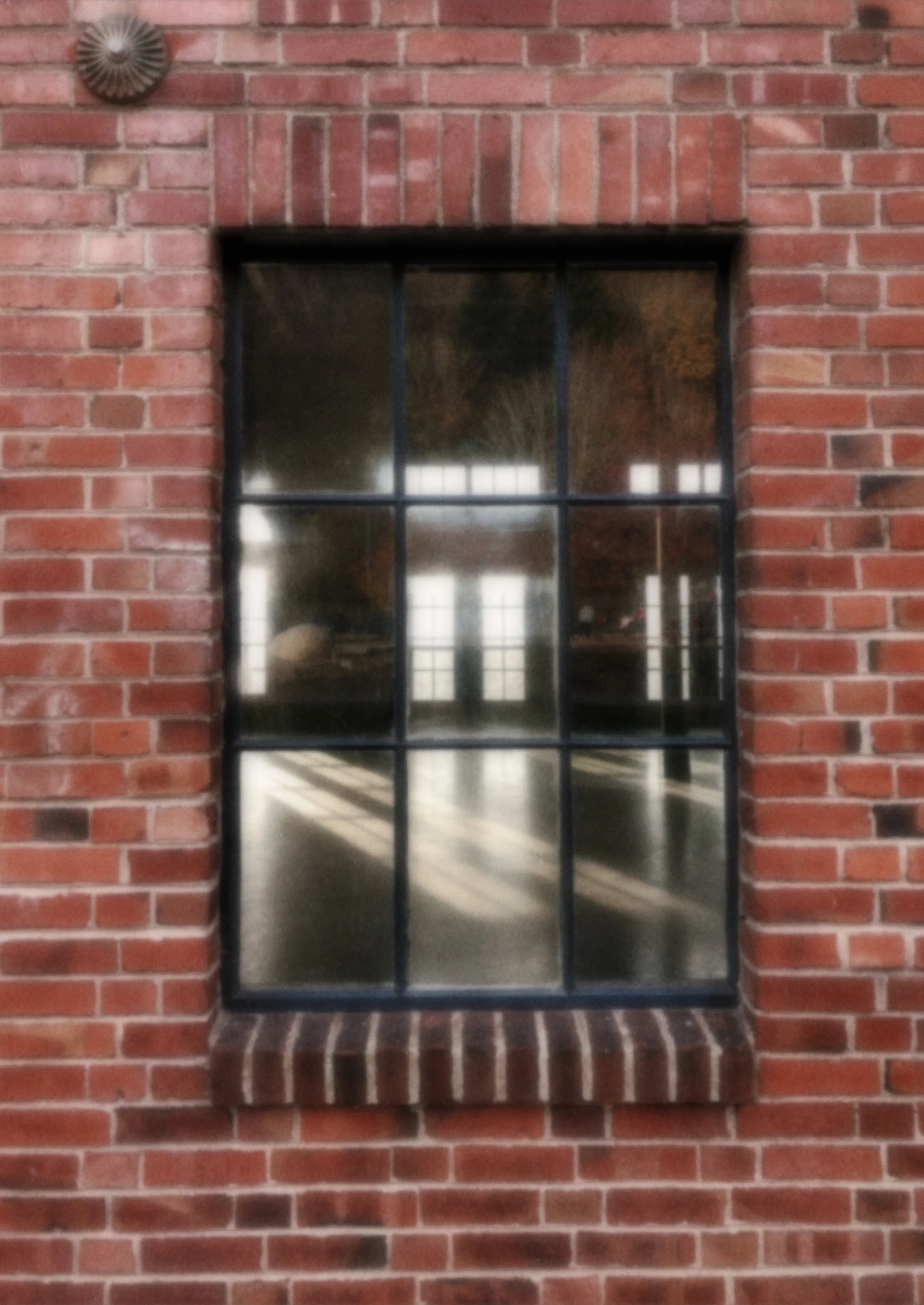 A black-framed window on a red brick wall. The window reflects the interior space with a bright light and some furniture or objects inside.