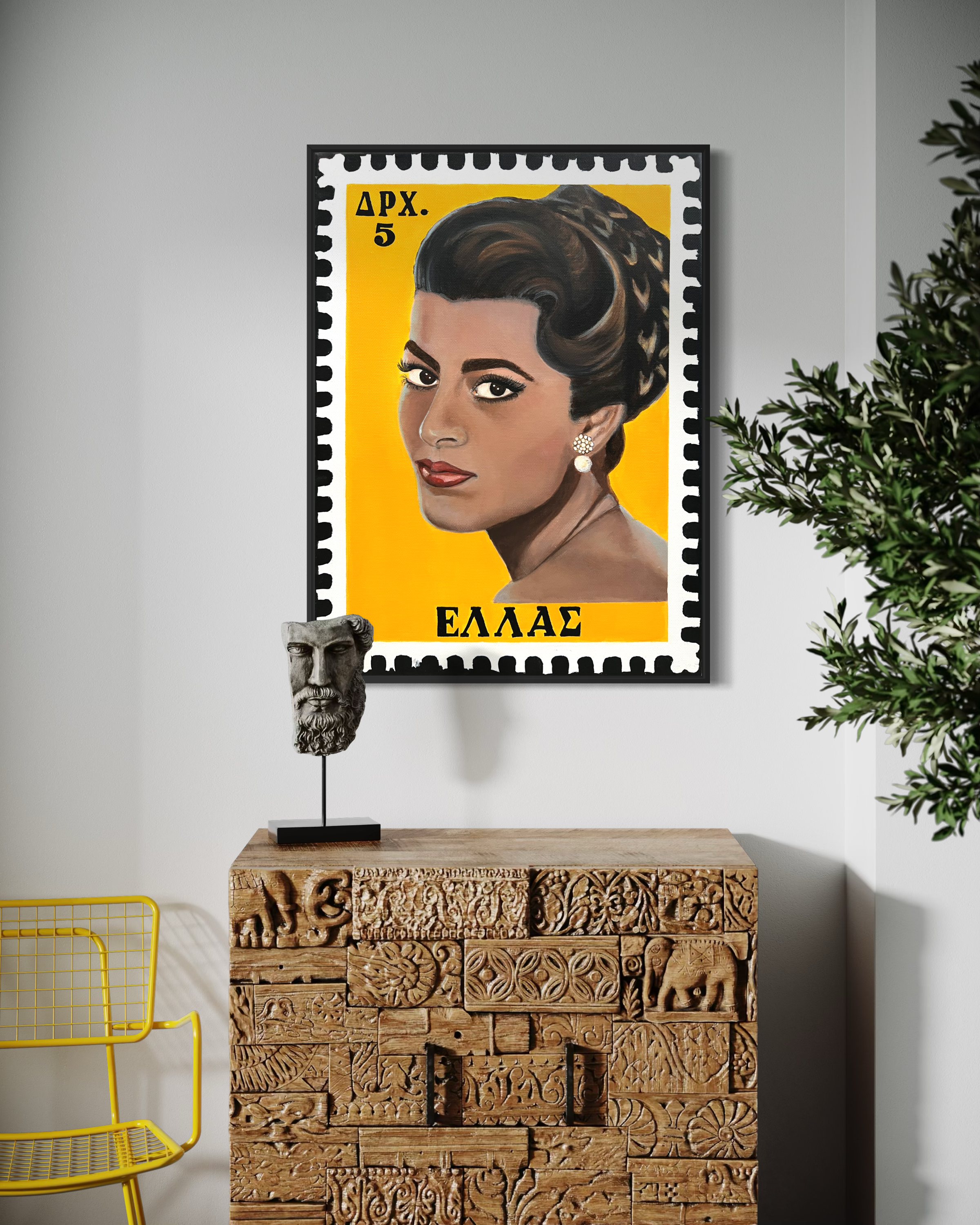 Interior scene with a yellow-framed Greek postage stamp portrait of a woman with dark styled hair and earrings, placed on a black frame, on a white wall next to a carved wooden cabinet and a green plant.