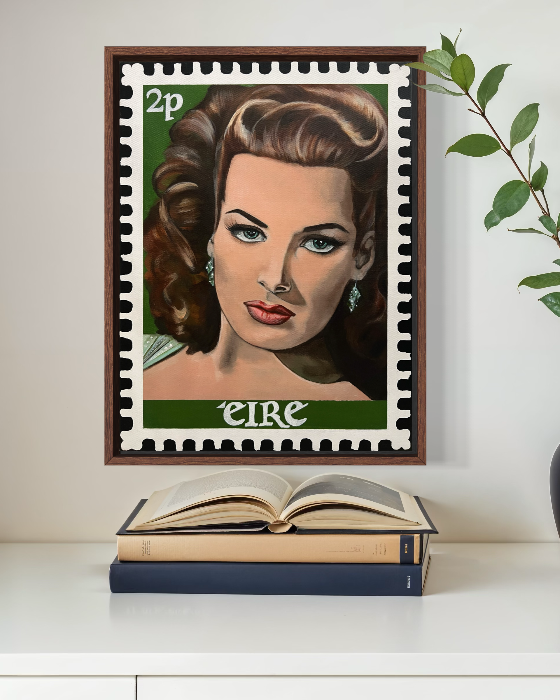 A framed postage stamp featuring a painting of a woman with brown, curly hair, blue eyes, and earrings, with the text '2p' and 'eire' partially visible. The stamp hangs on a plain wall to the right of a leafy plant. Below the stamp, there is an open 