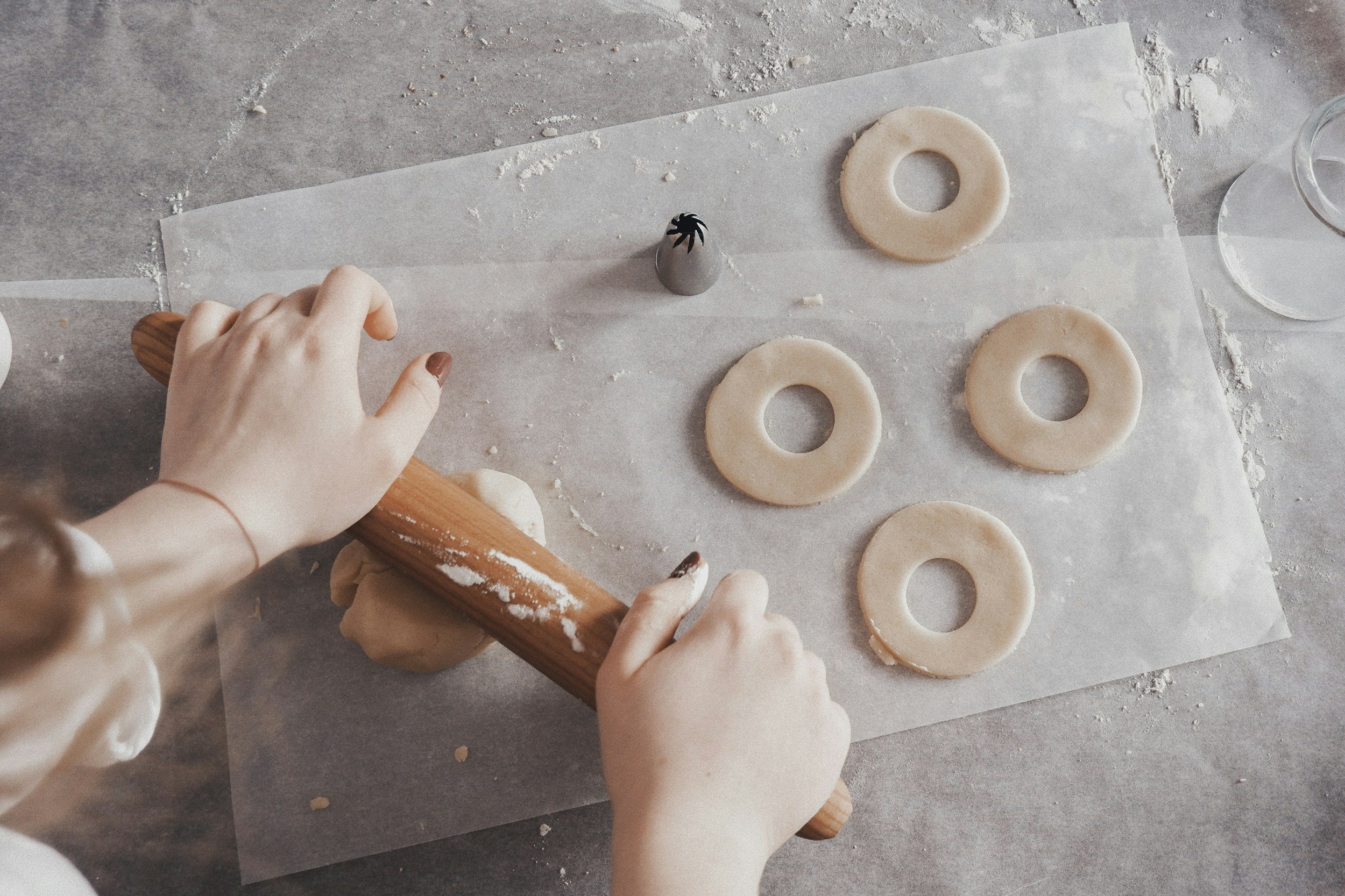 Child rolling out cookie dough with a wooden rolling pin on parchment paper, with cookie cutters nearby.