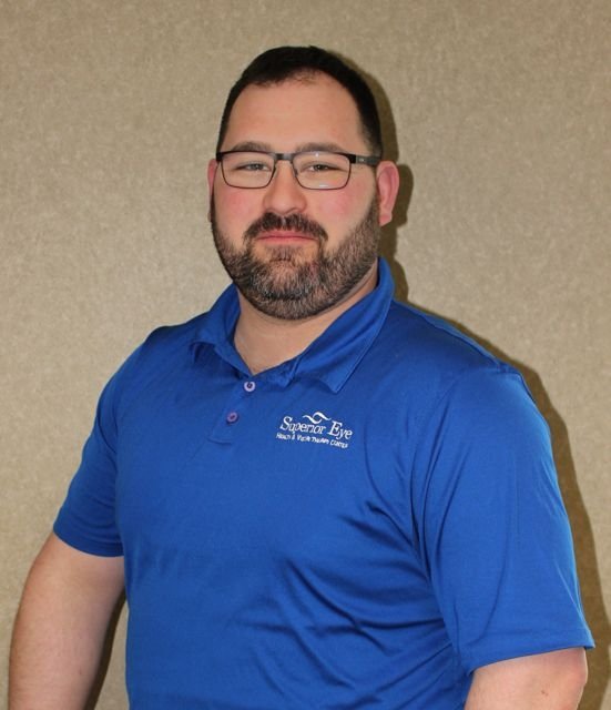 A man, Dr. Stephen Herman, with glasses and a beard wearing a blue polo shirt and standing in front of a beige wall.