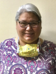 Smiling woman with short gray hair and glasses, wearing a paisley-patterned blouse and a yellow face mask around her neck. She is a Vision Therapy graduate from Superior Eye Health.