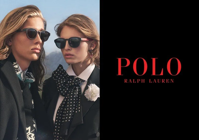 Two women wearing sunglasses and black outfits with polka dot accessories, standing outdoors, with a Polo Ralph Lauren advertisement featuring the brand name in red and models on a black background.