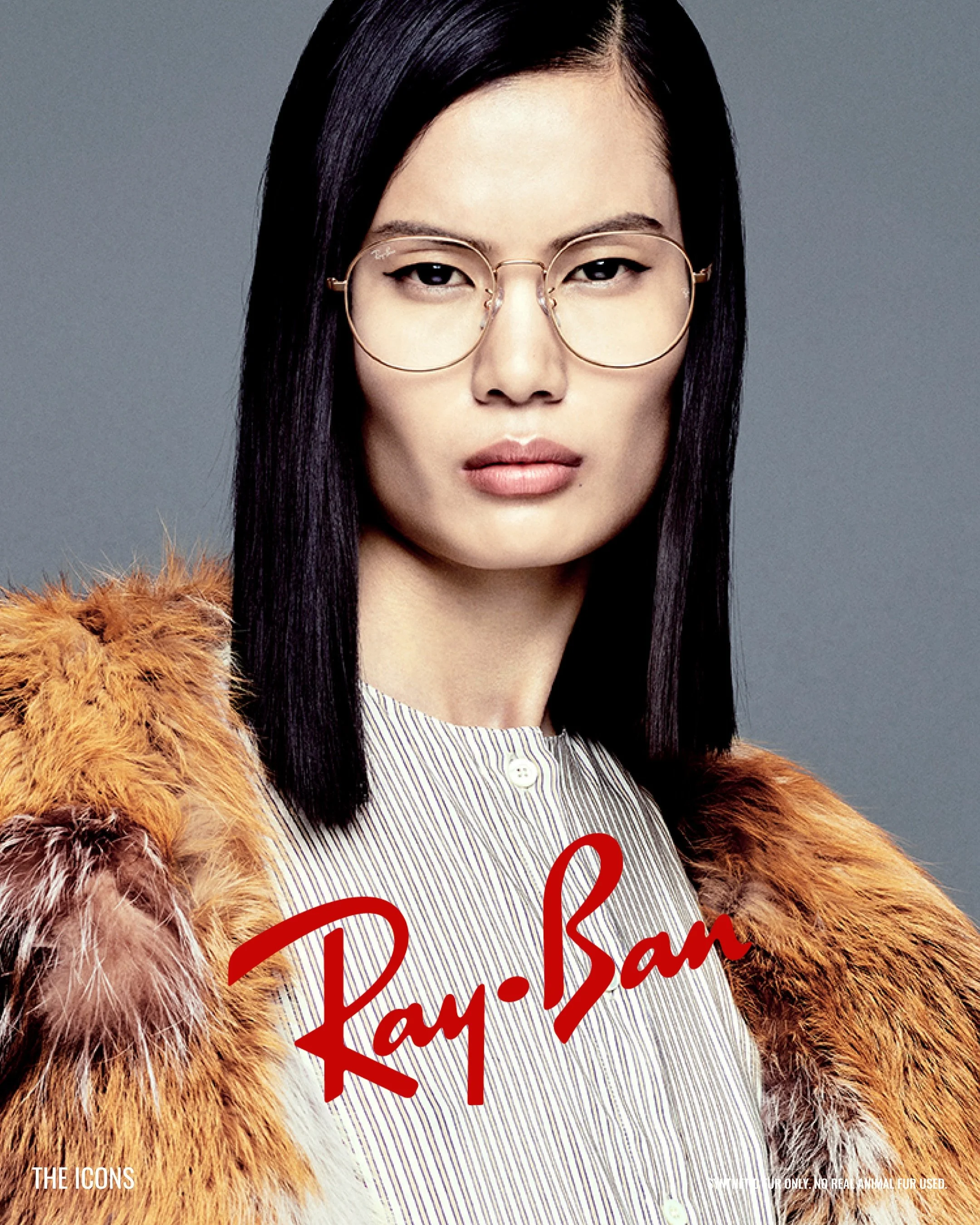 A woman with long black hair wearing large round glasses and a fur coat over a striped shirt, with red handwritten text overlay and a gray background.