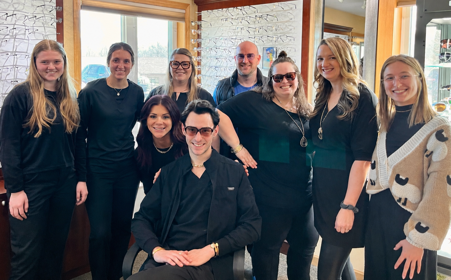 Group of 10 people smiling and posing for a photo inside a eyewear store.