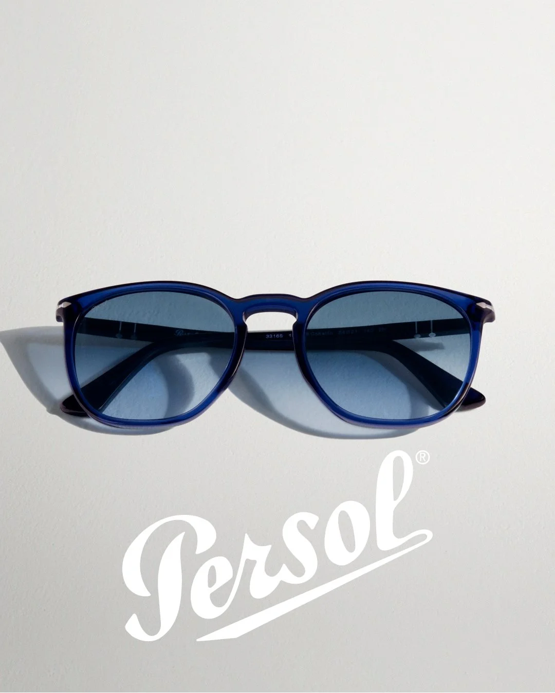 Blue sunglasses with dark lenses and Persol logo on a white surface