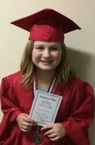 Young girl in a red graduation gown and cap holding an award certificate and wearing a medal. She is a Vision Therapy graduate from Superior Eye Health.