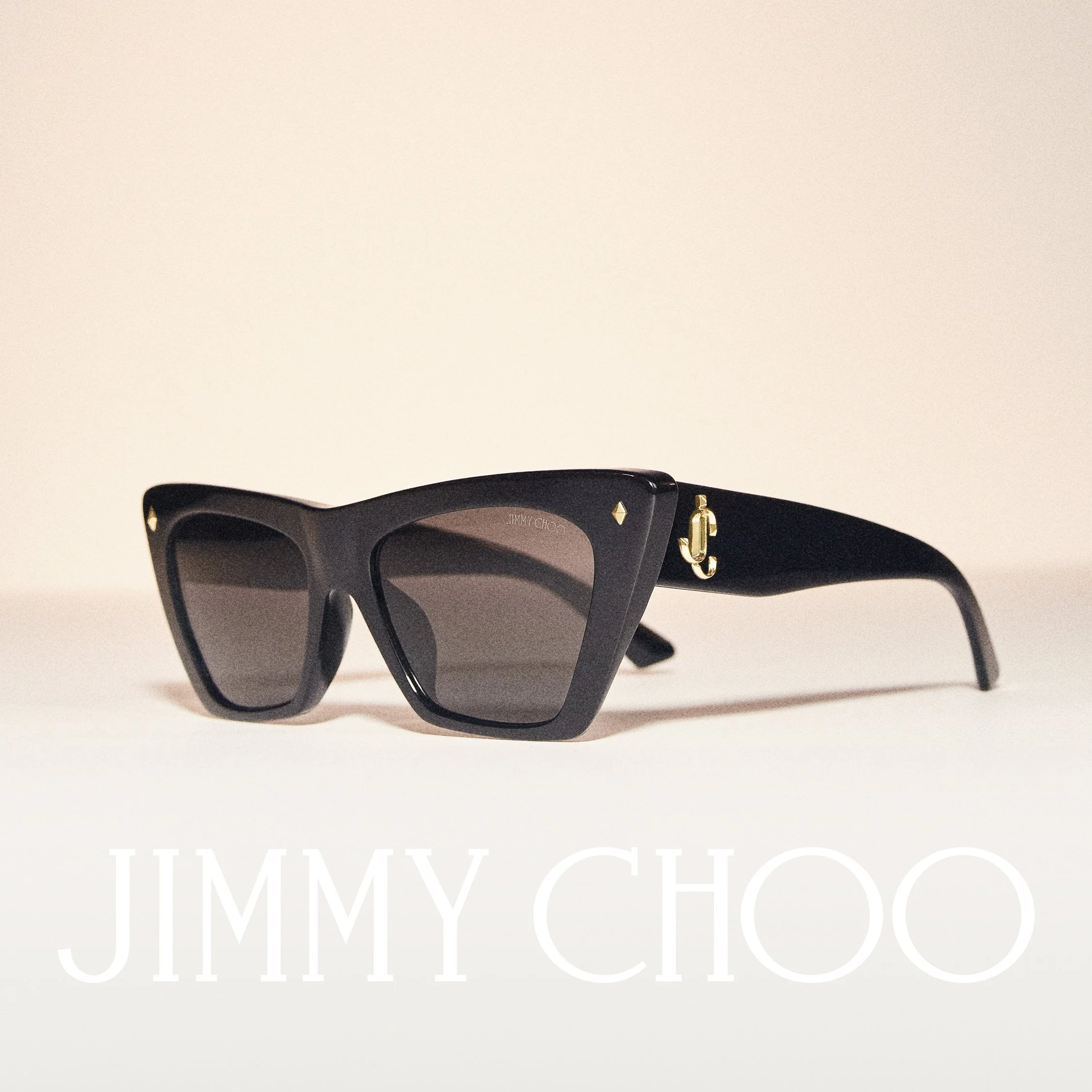 Close-up of black sunglasses with gold accents on a white background, with text partially visible reading 'JIMMY CHO' at the bottom.