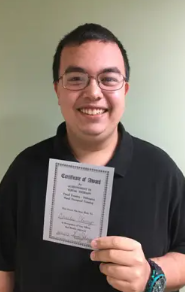 A young man with glasses smiling and holding a certificate of achievement. He is a Vision Therapy graduate from Superior Eye Health.