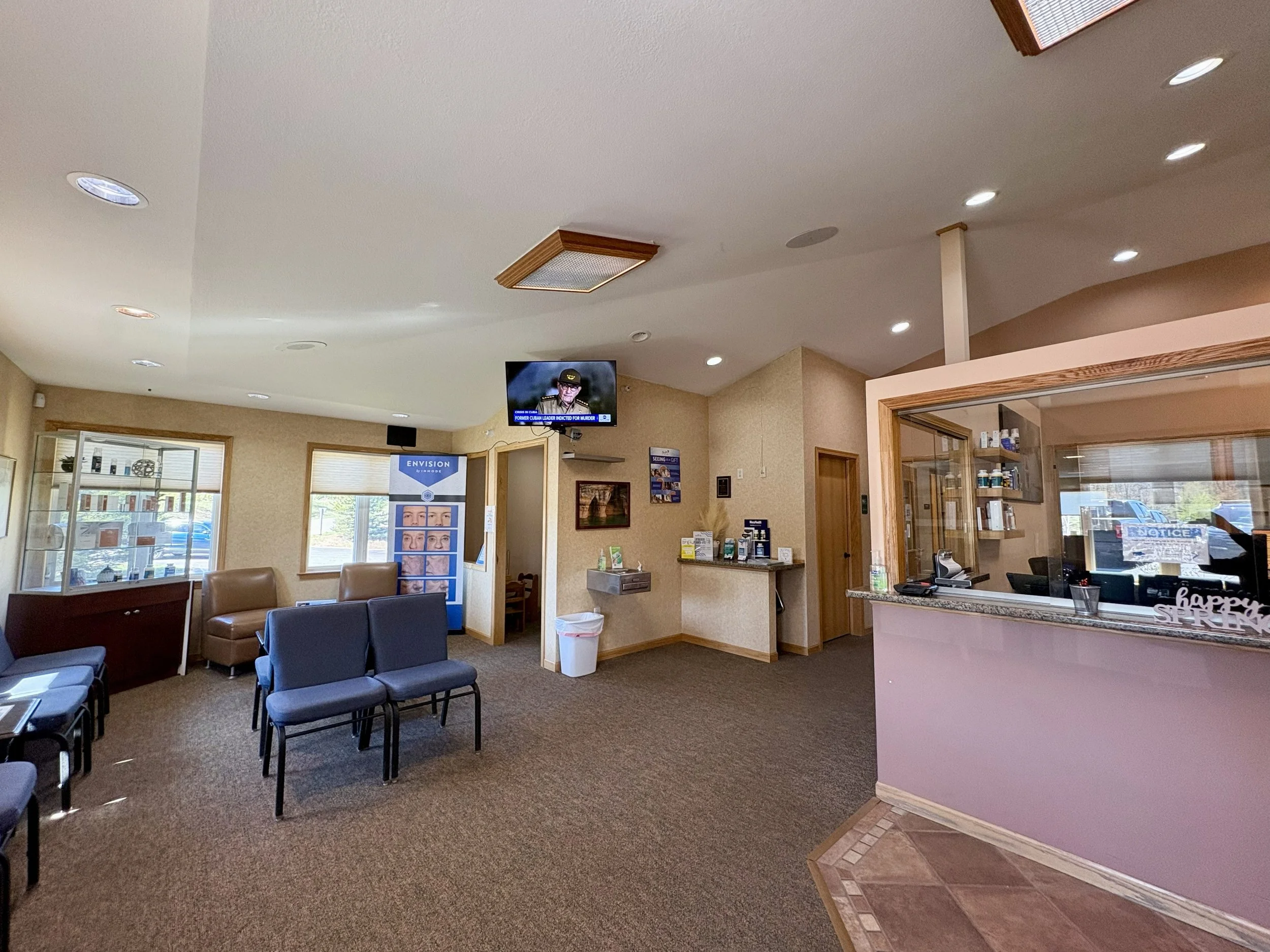 Interior view of a waiting room with chairs, a reception desk, and a television mounted on the wall.