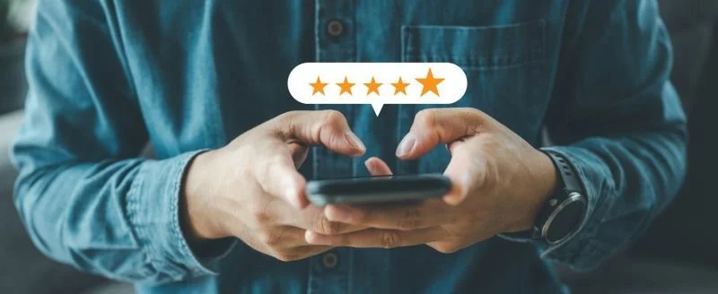 Person in denim shirt holding smartphone with a five-star review graphic above