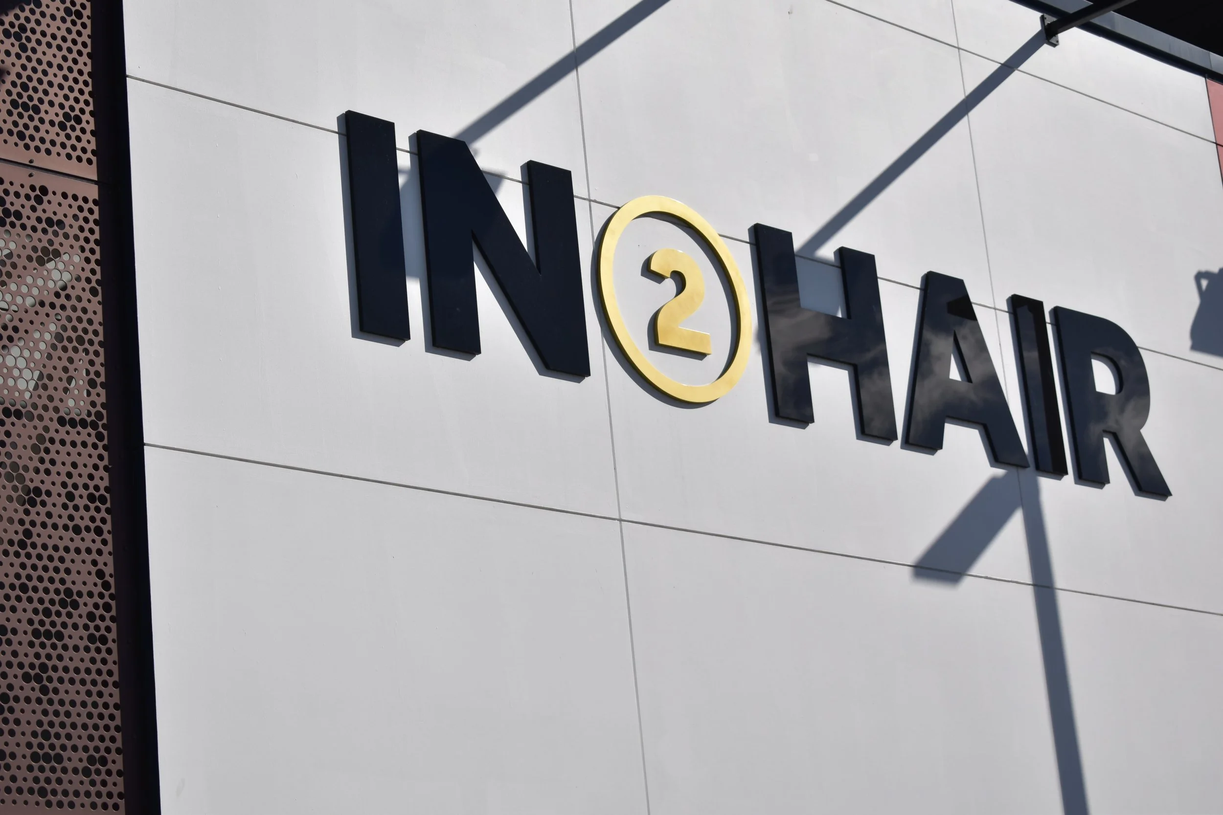 Signboard and shop front signage  with the text 'IN2HAIR' in black letters on a white wall, with the number 2 in a yellow circle as part of their signature logo.