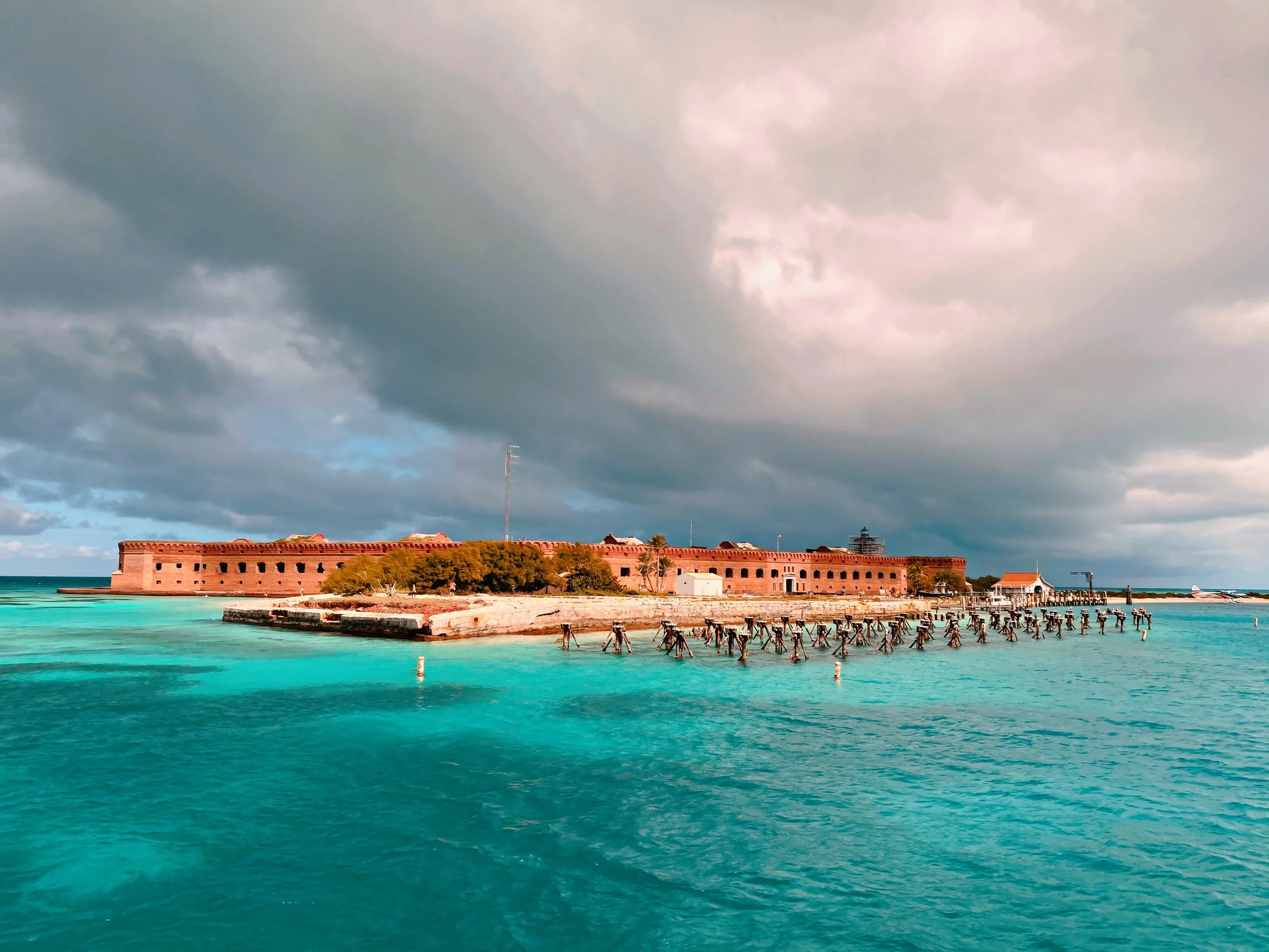 An old fort situated on a small island surrounded by turquoise water, with a cloudy sky overhead.