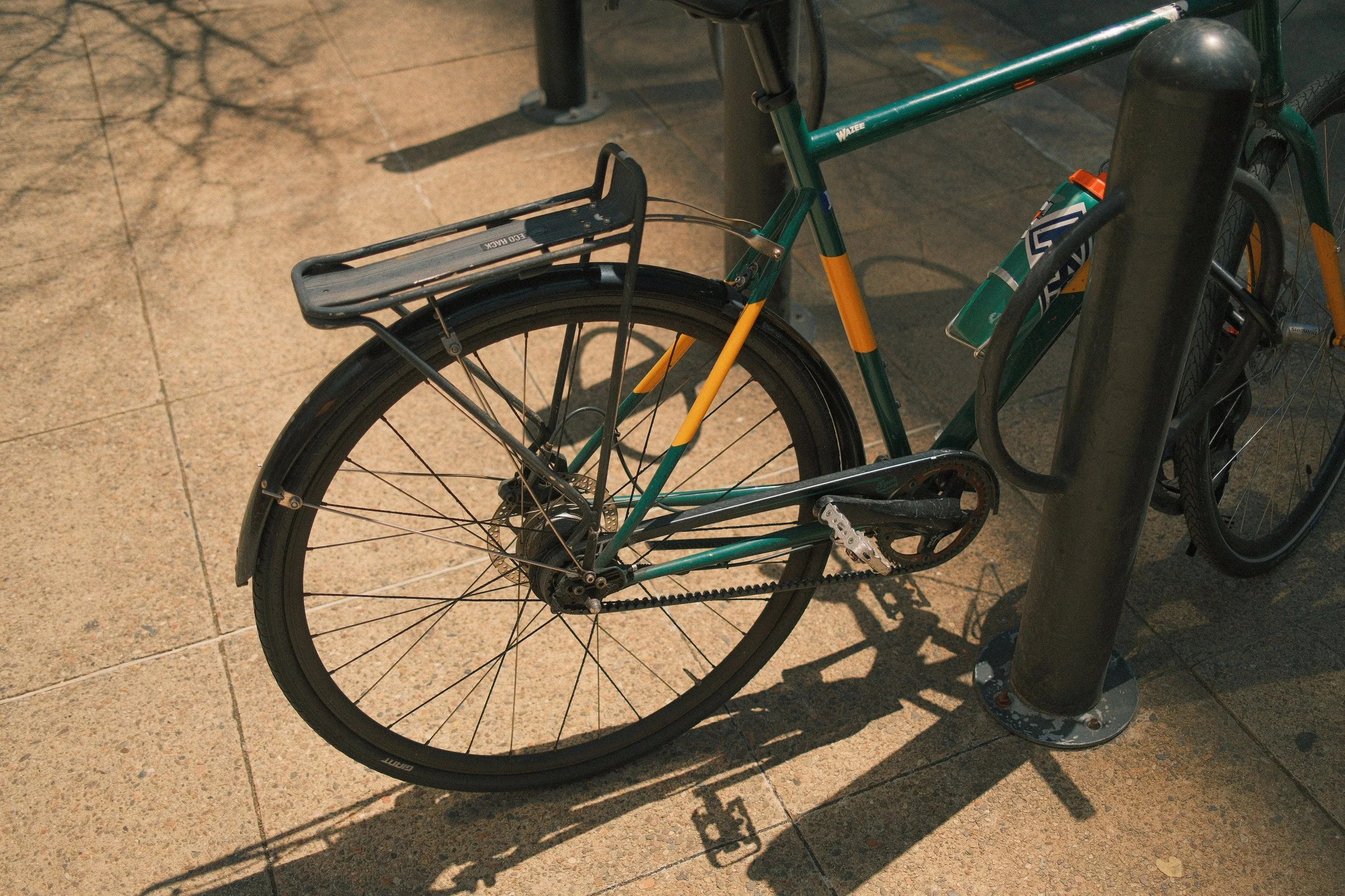 Green and yellow bicycle locked to a black bike rack on a tiled sidewalk.