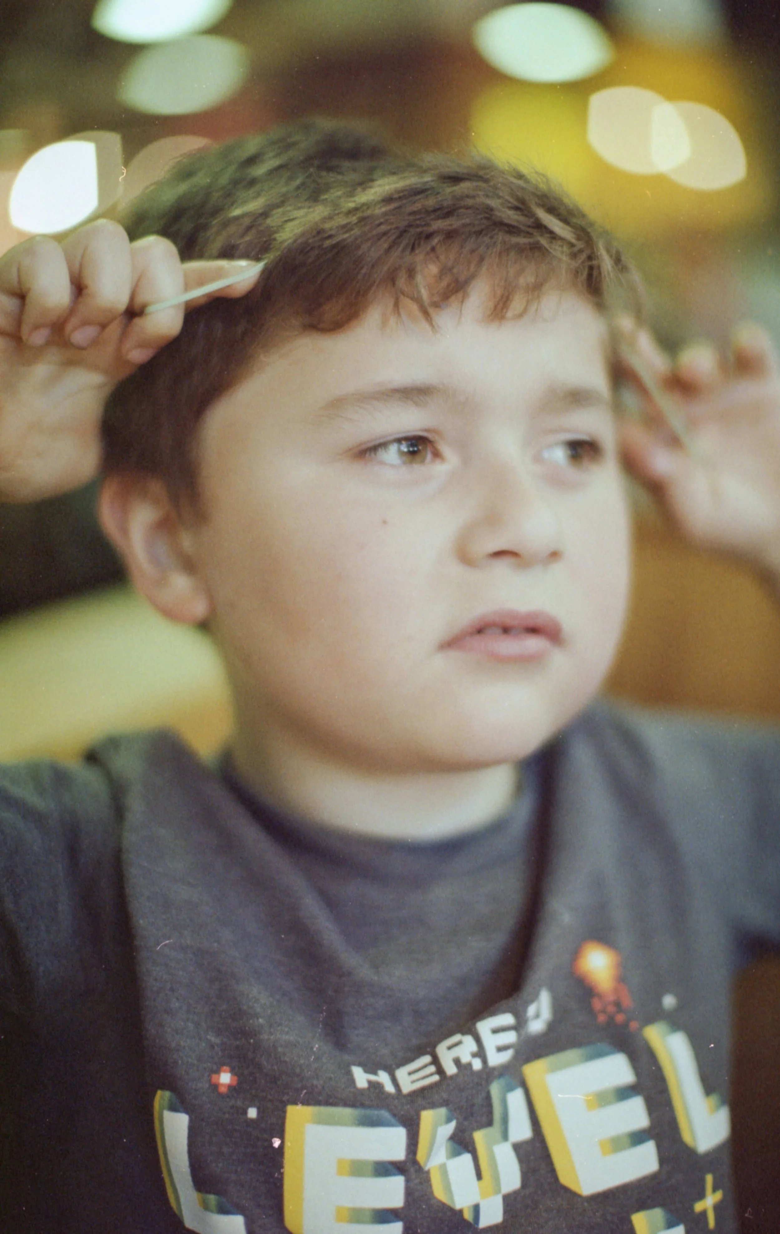 A young boy is getting a haircut at a salon, with scissors and a comb in the hairdresser's hands.