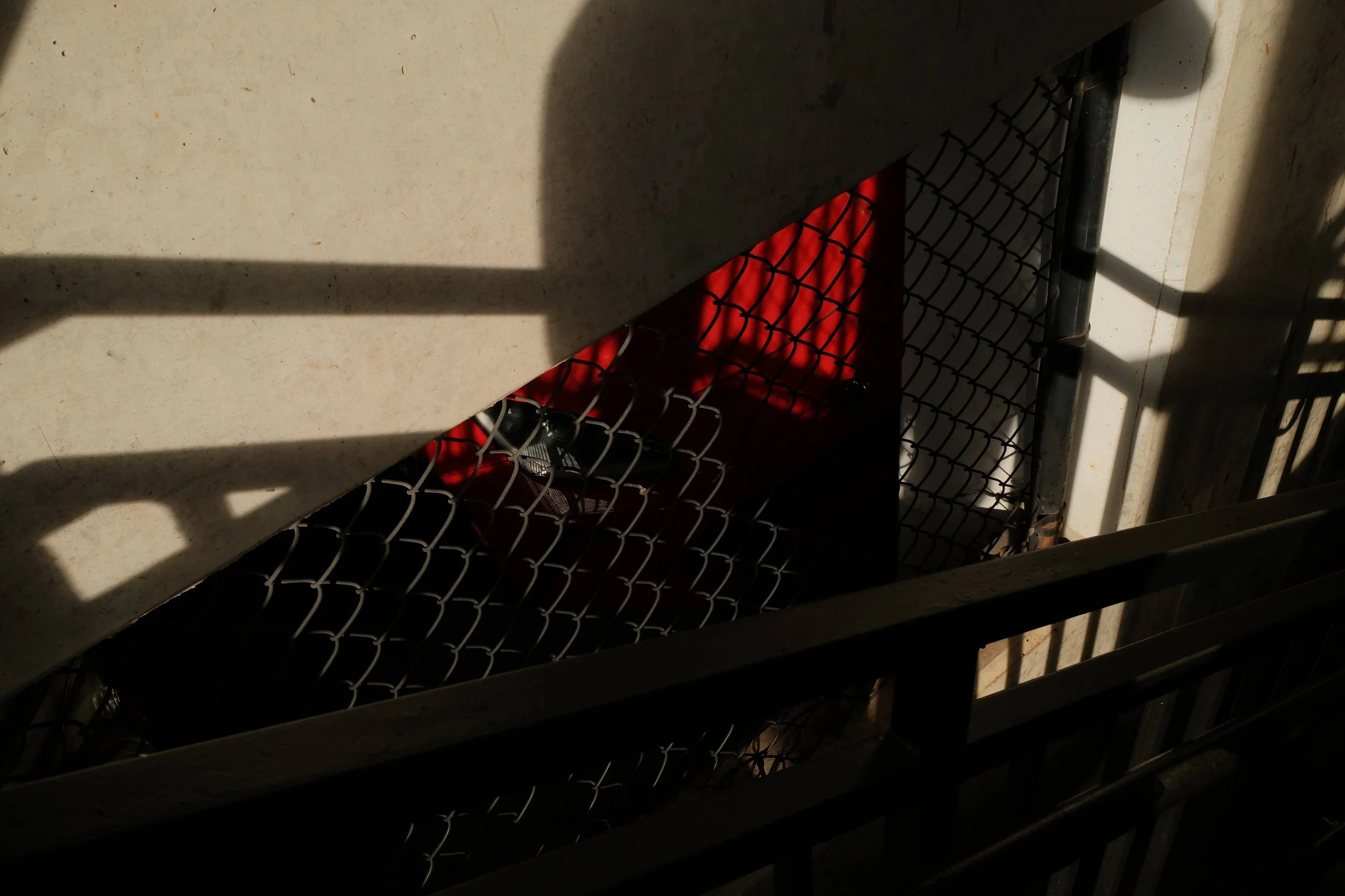 Close-up of a small outdoor patio space with a chain-link fence, a red wall in the background, and a few shoes, including a purple sneaker, on the ground.
