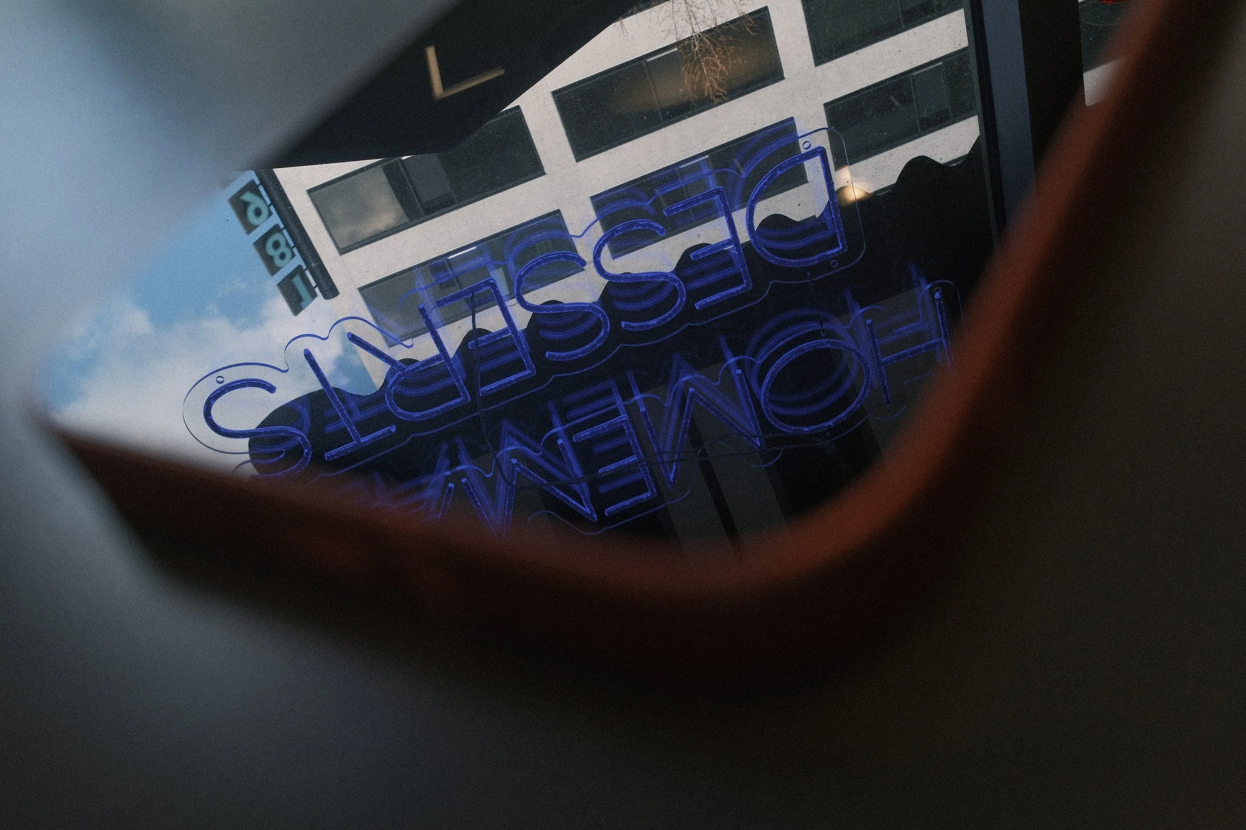 Reflection of a building and a blue neon sign that reads 'Business' and 'Home' seen through a round mirror.