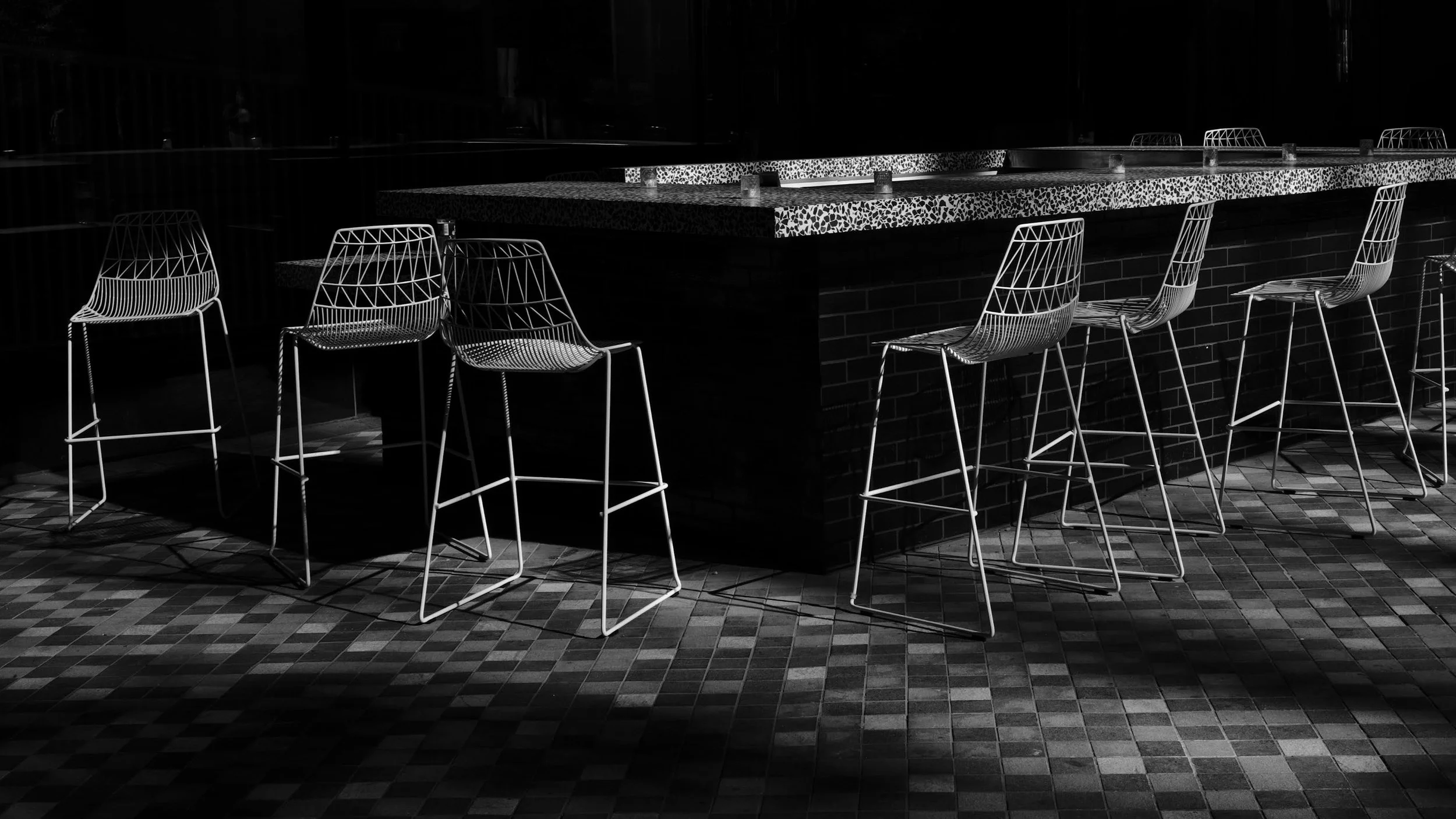 Empty bar with high wireframe chairs, dim lighting, black and white photo.