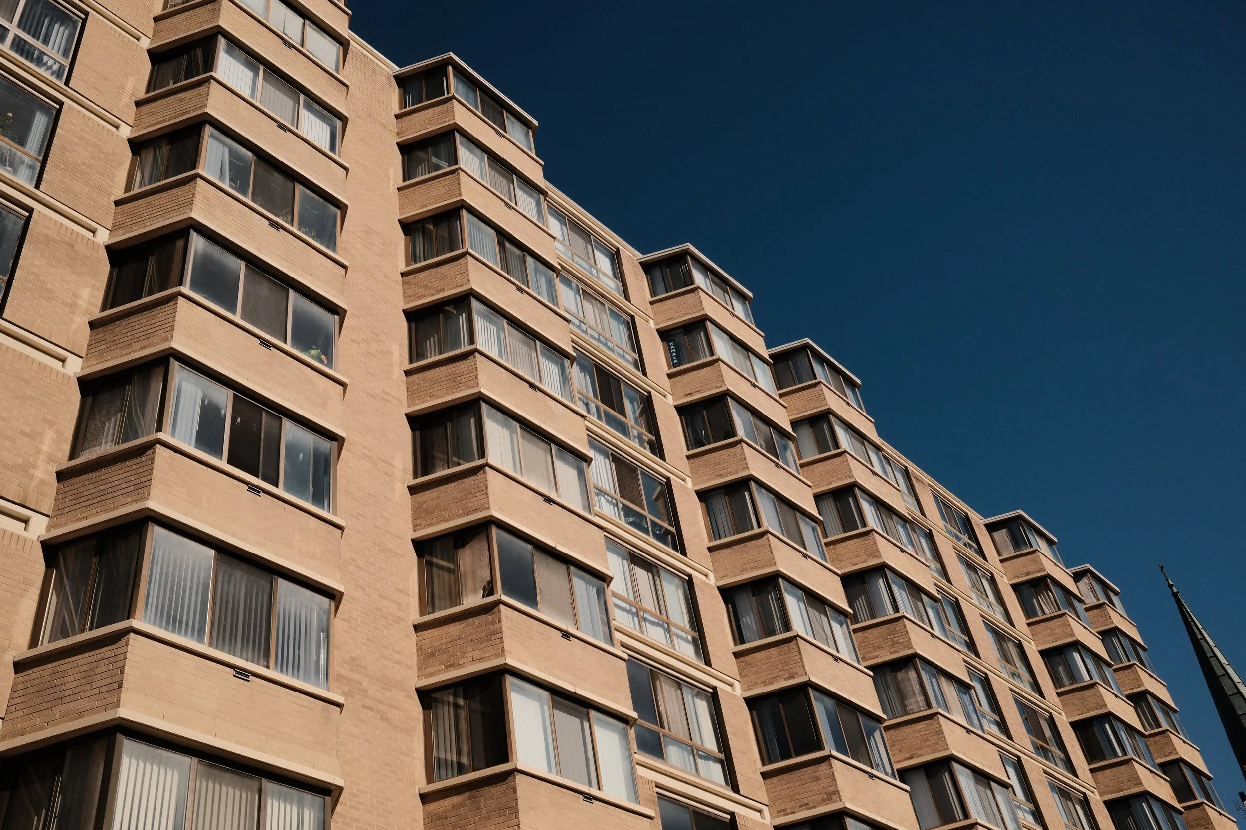 A tall apartment building with multiple windows, set against a clear dark blue sky.