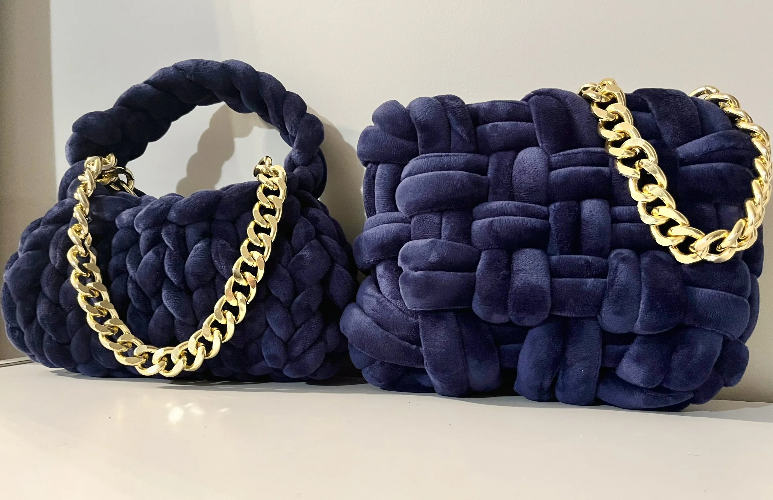Two navy blue velvet handbags with thick braided handles and gold chain accents, placed on a white surface.