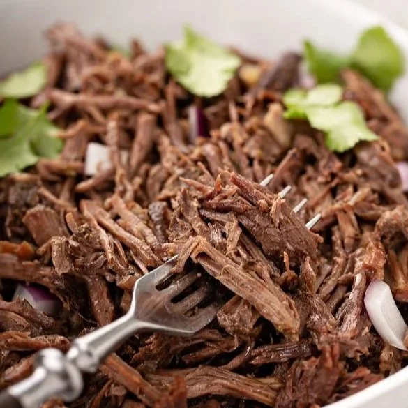 From above hands of unrecognizable woman rubbing aromatic spices into piece of raw meat over parchment paper