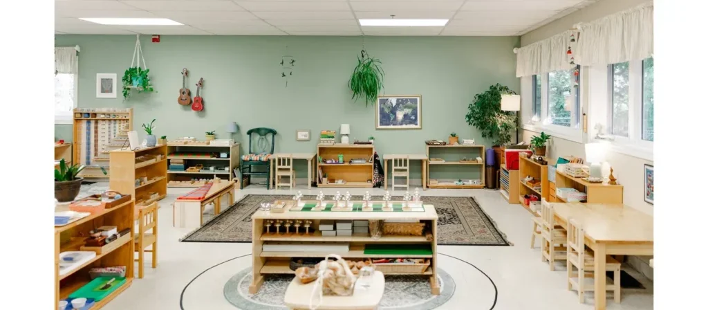 A classroom with educational toys and furniture, green plants, and artwork, featuring a large window providing natural light.