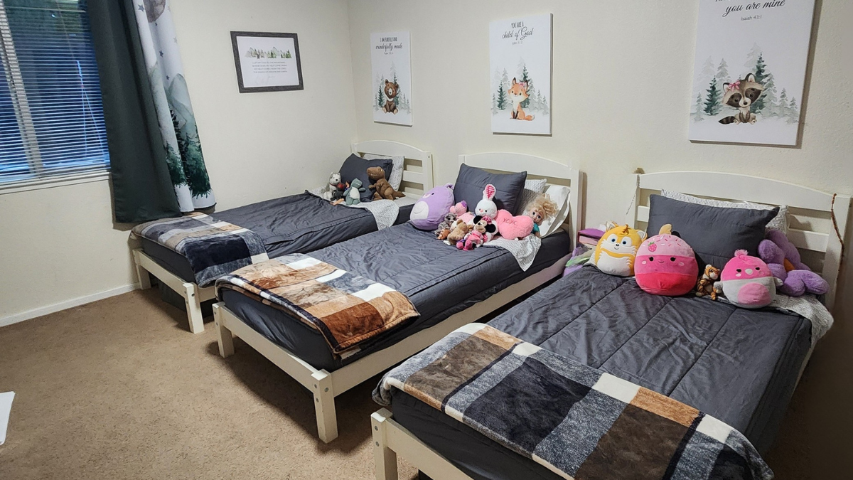 Kids shared bedroom with three twin beds, simple bedding, neutral colors, and budget-friendly small-space setup.