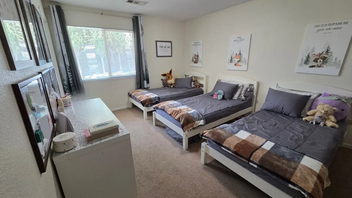 Shared bedroom for three kids with three individual beds arranged along the walls and matching bedding.