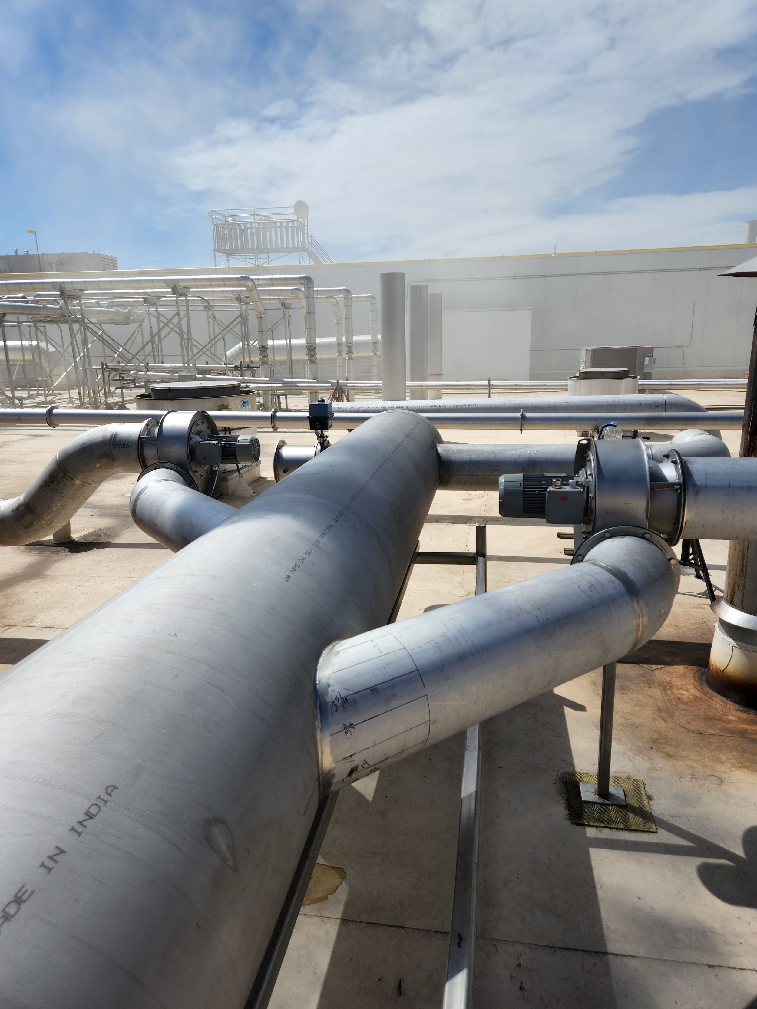 Industrial rooftop with large metal pipes and machinery under a partly cloudy sky.