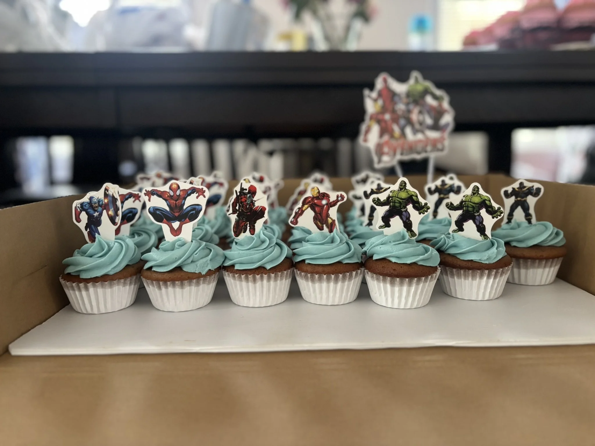 Cupcakes with blue frosting decorated with Marvel superhero toppers including Spider-Man, Hulk, and Captain America.