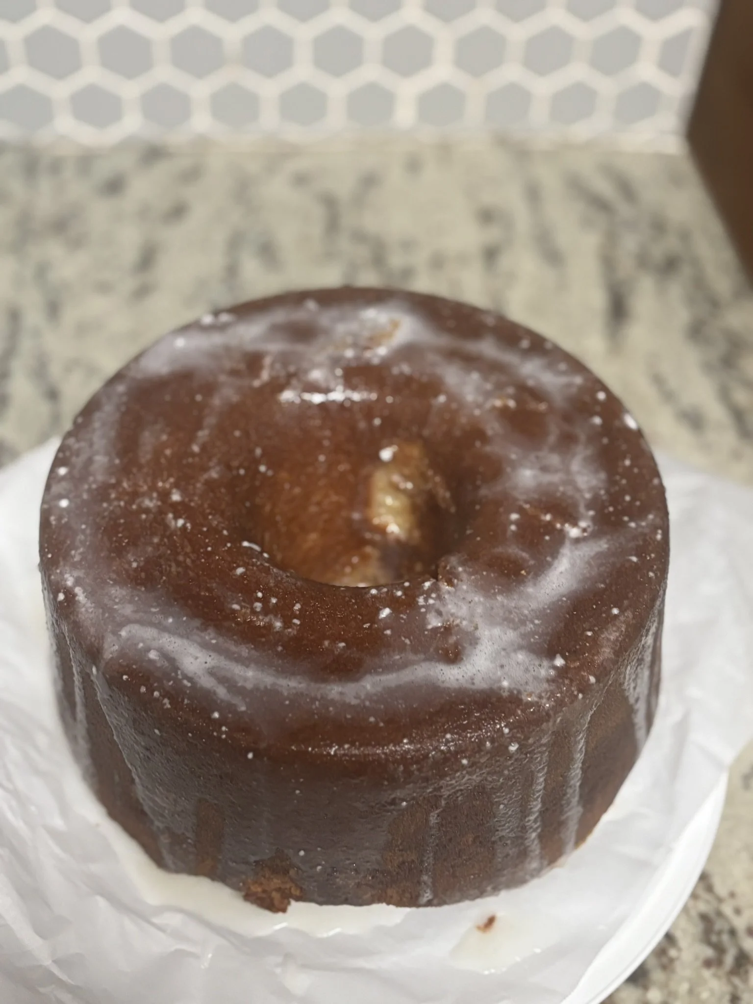 A small, round, chocolate cake with a hole in the center, covered in glossy chocolate glaze, sitting on a white napkin.