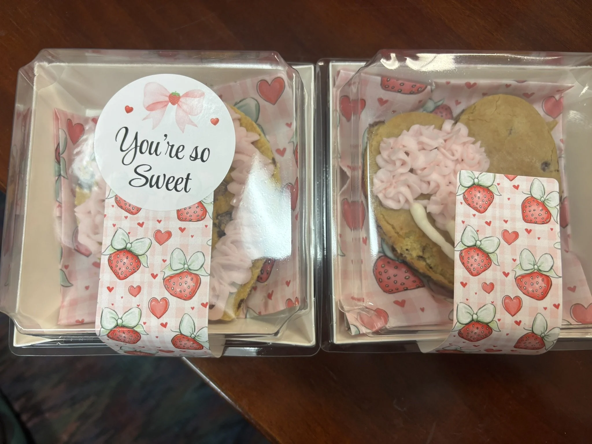 Two boxes of cookies decorated with pink and strawberry-themed stickers and pink frosting, one with a sticker that says 'You're so Sweet.'