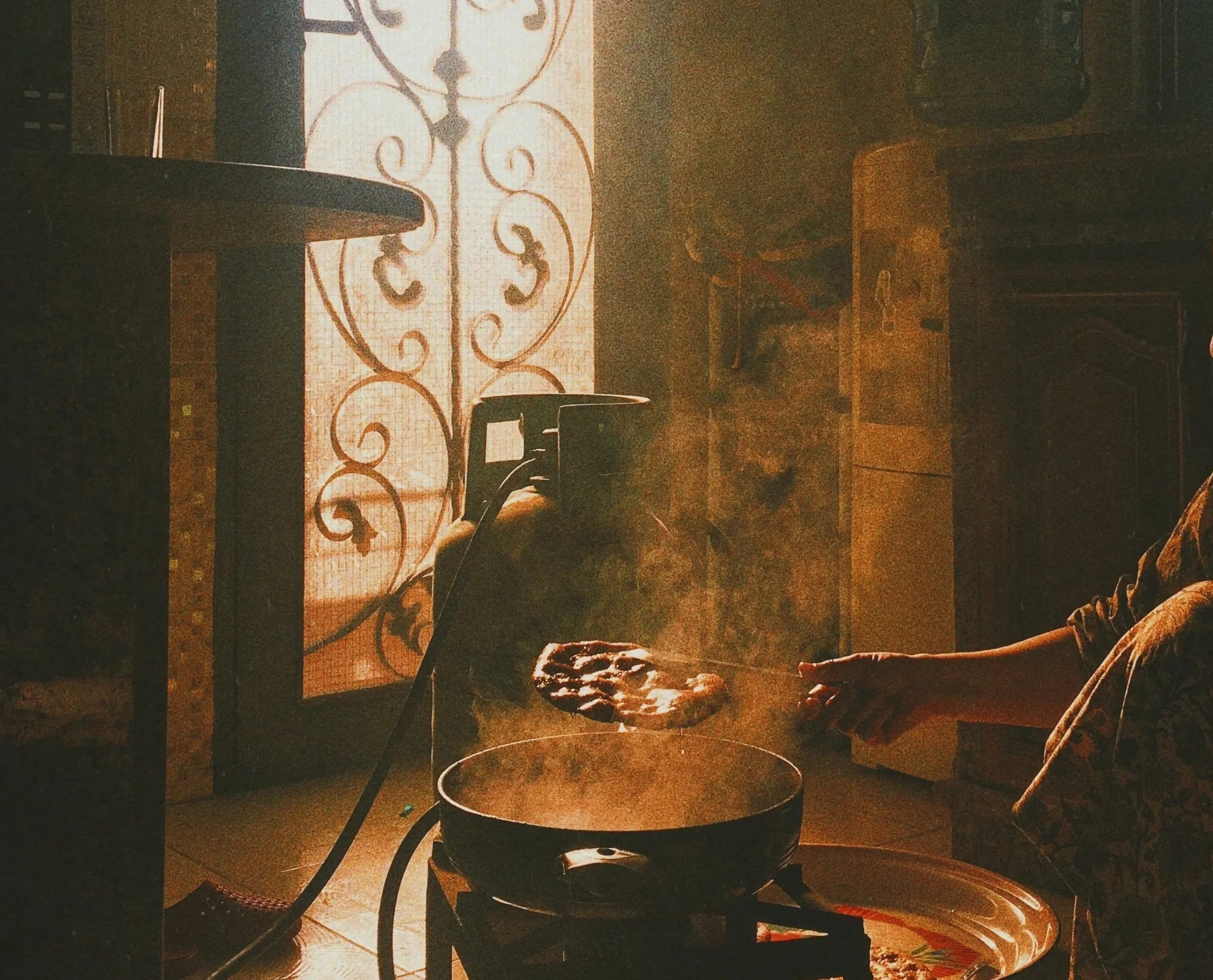 Person cooking on a stove in a dimly lit kitchen with a patterned glass door in the background.