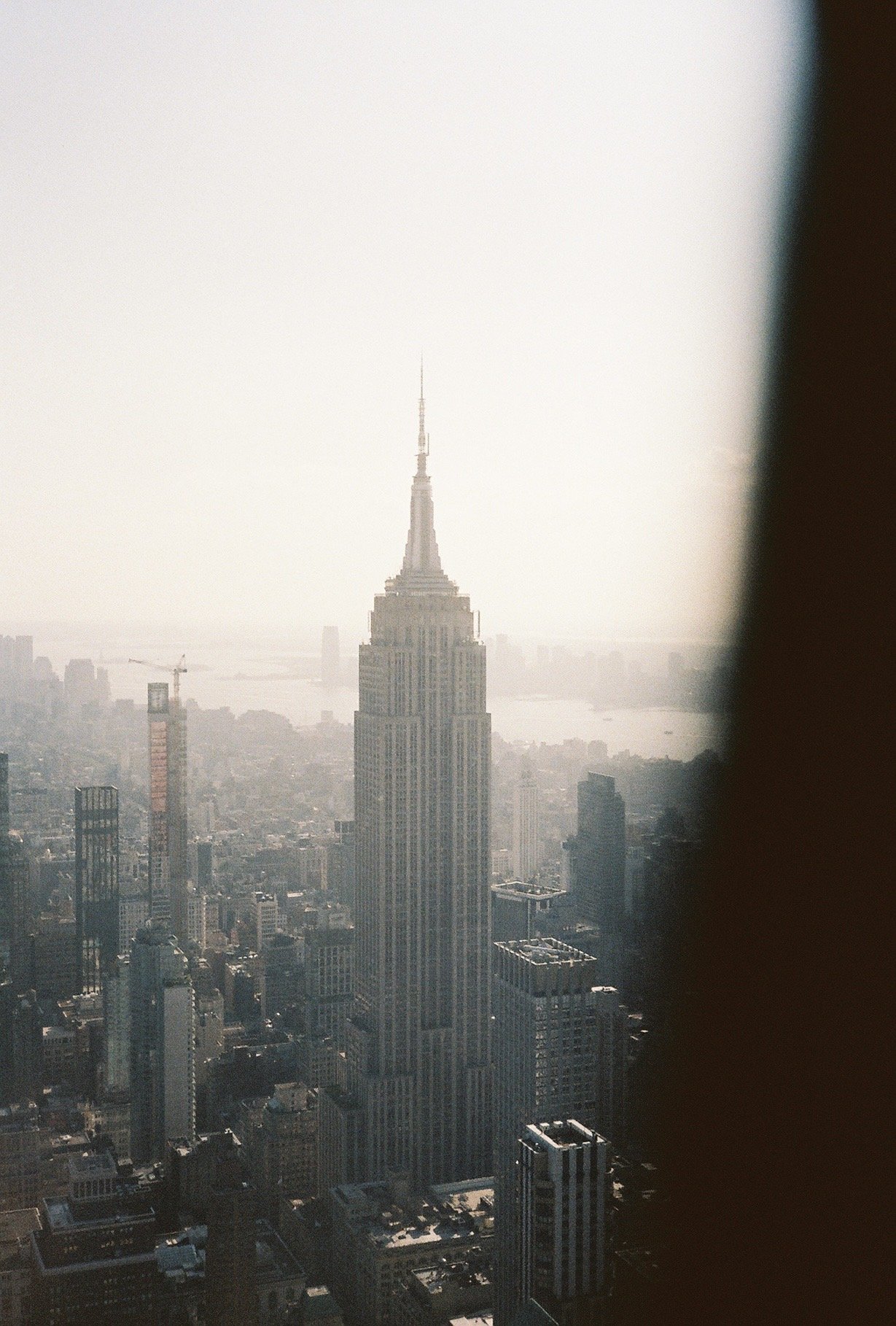 View of the Empire State Building in New York City through a window, with part of the window frame visible on the right side.