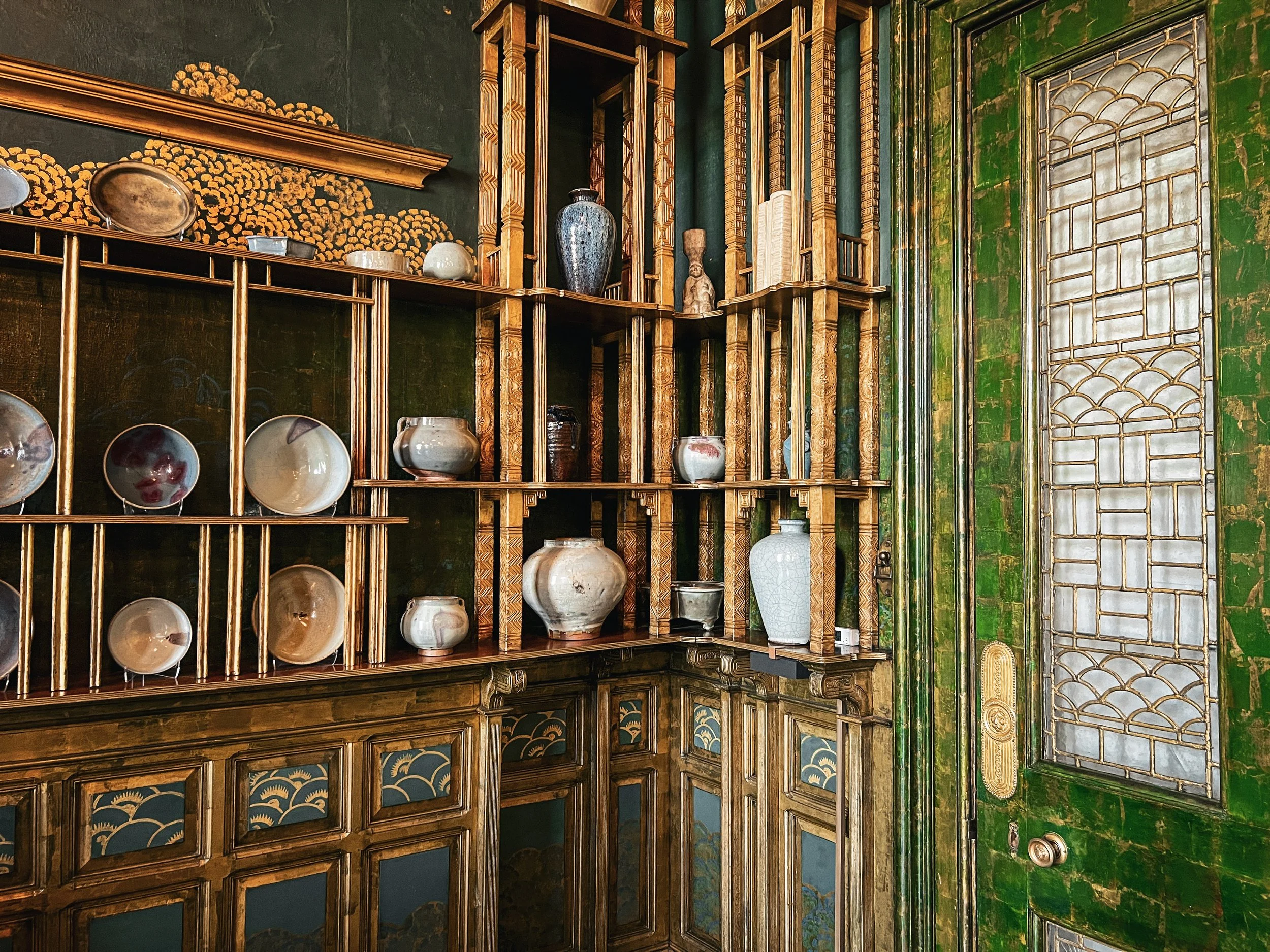 Antique porcelein against green patina walls displayed on weathered bamboo shelving. iPhone 