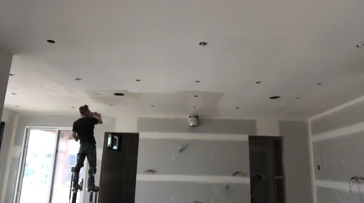 A person standing on a ladder working on a ceiling in a room under construction or renovation.
